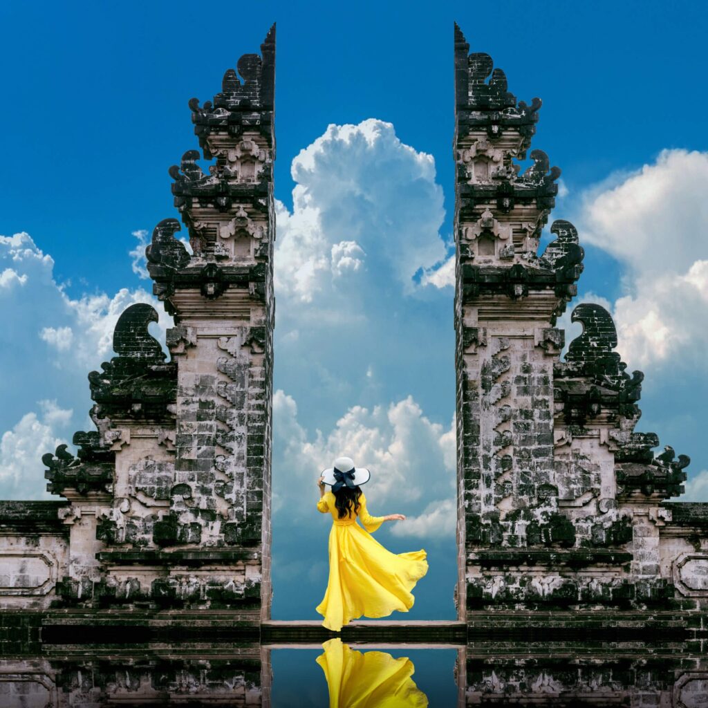 A woman in a yellow dress stands in front of an old temple archway during her holiday in Indonesia.