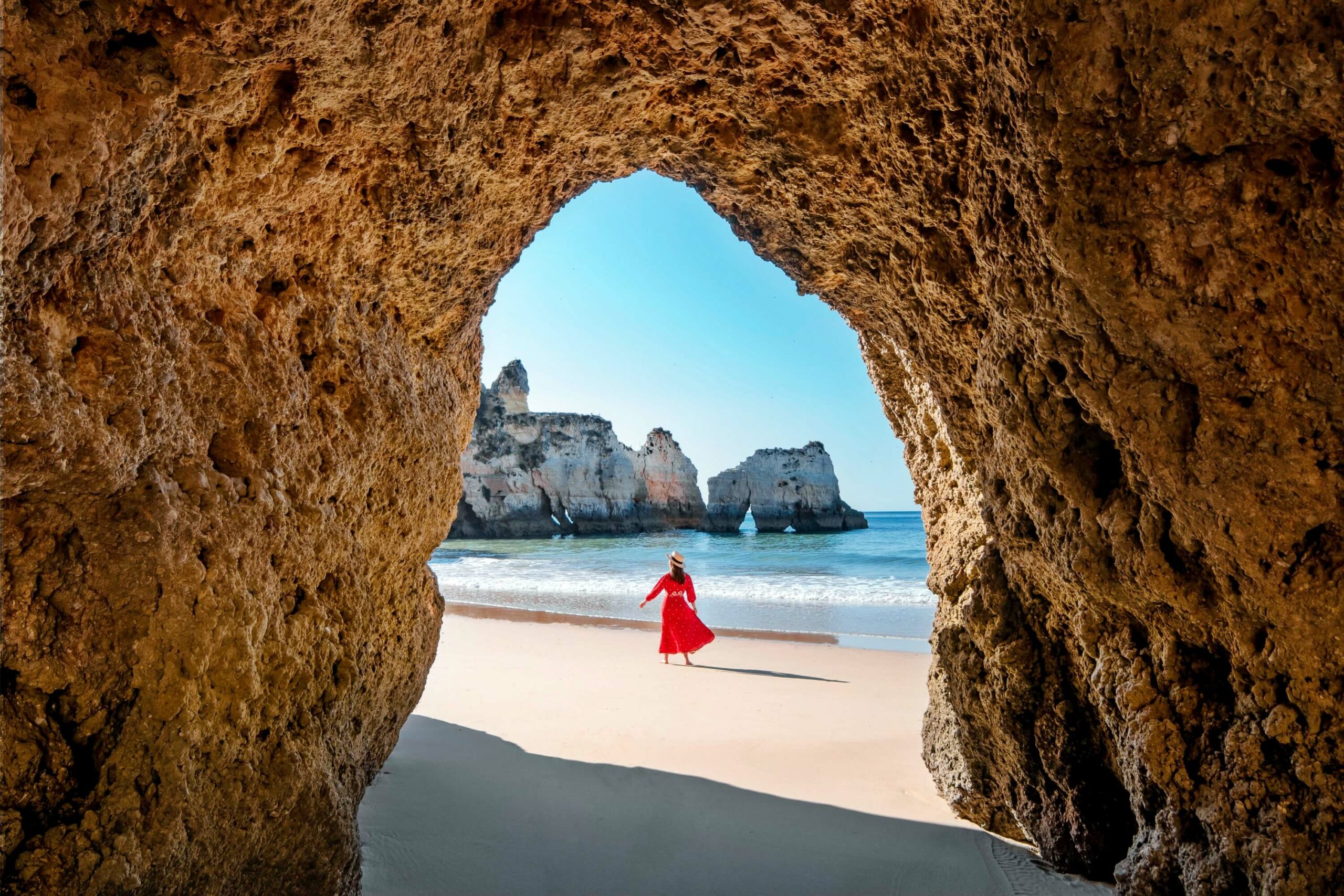 A woman in a red dress exploring a cave by the beach on her holiday.