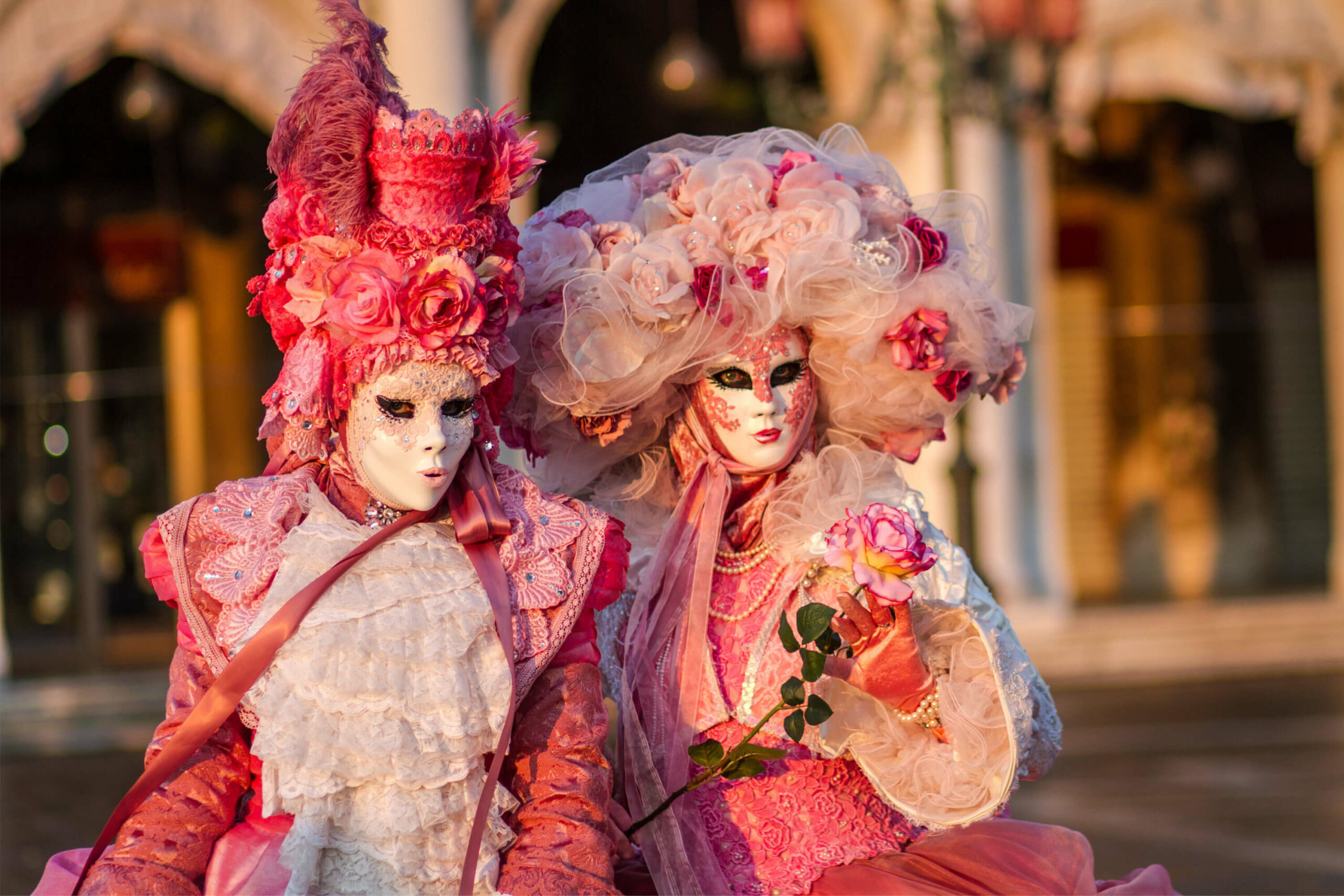 Two people dressed in pink costumes and wearing masks are wandering down a street in Venice, Italy during the Carnival.