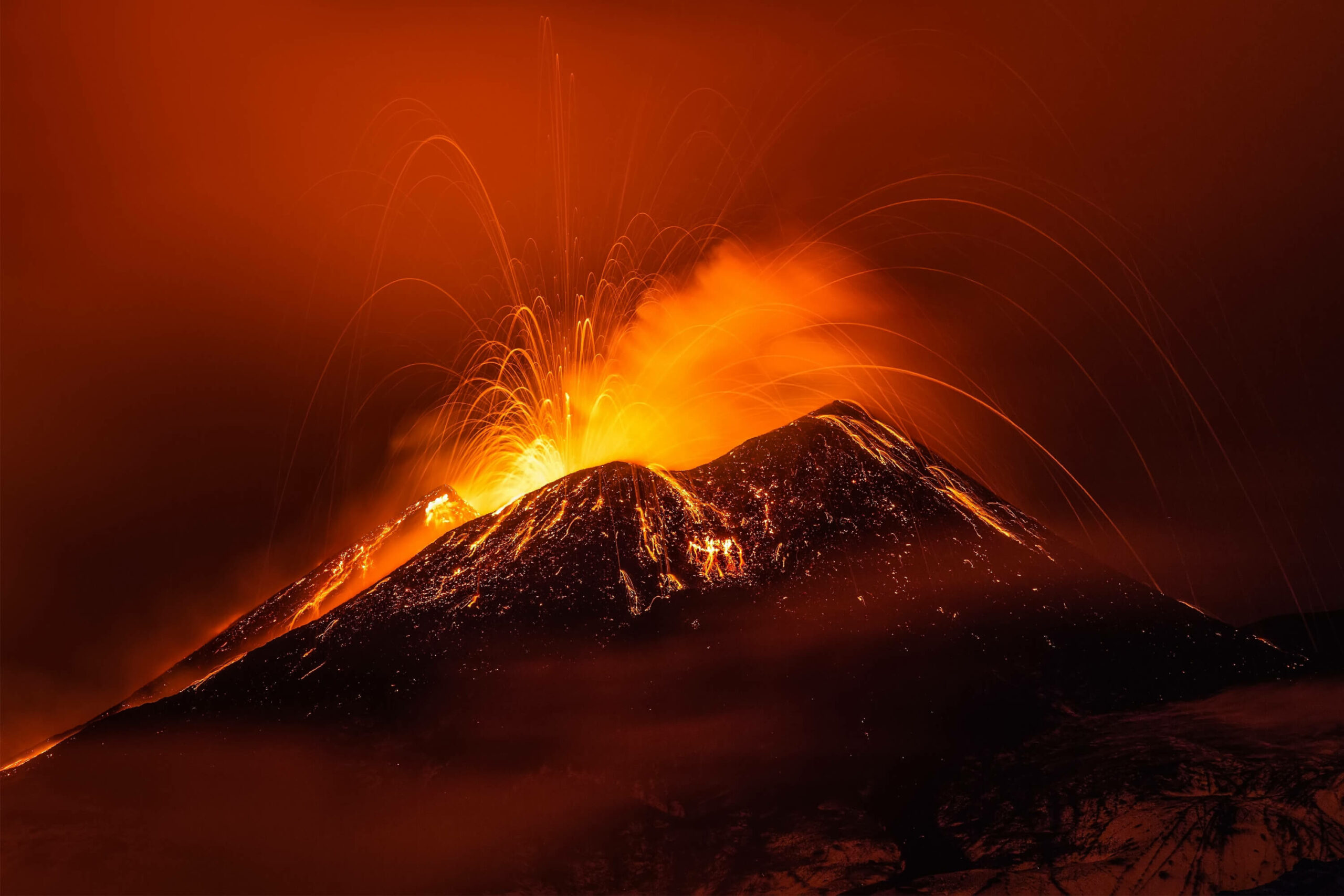 A volcano is lit up at night with orange smoke, an exciting sight for adventure travel enthusiasts.