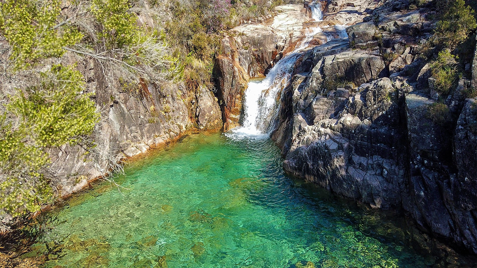 Small lagoon between rocks, with waterfall and green and crystal clear water