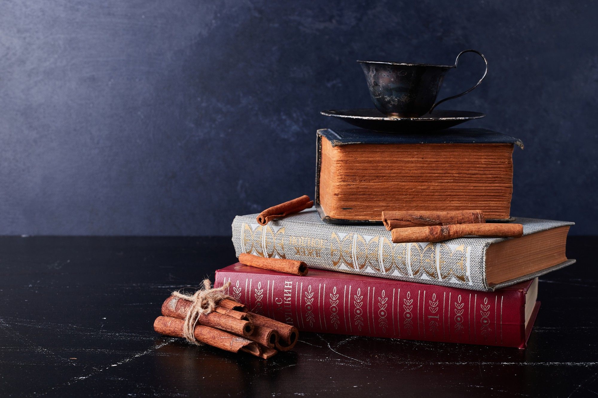 Old pile of books with a teacup on top of them and cinnamon sticks