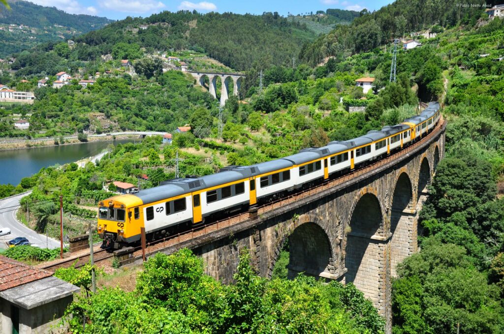 Old train on top of an old stone bridge surrounded by green hills and river.