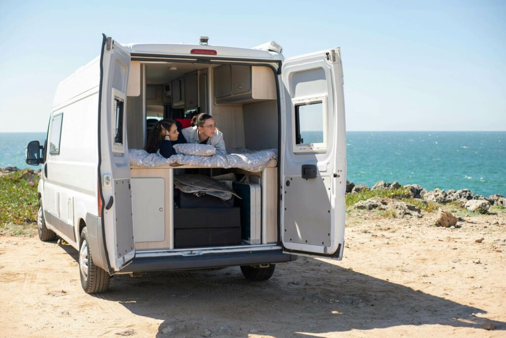 Campervan by the coastloine, standing on a cillf, with two people inside smiling and talking