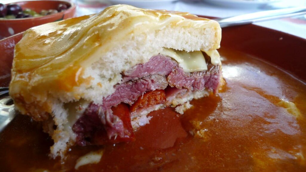 bread with layers of different types of meat inside, covered in sauce and served on  a plate