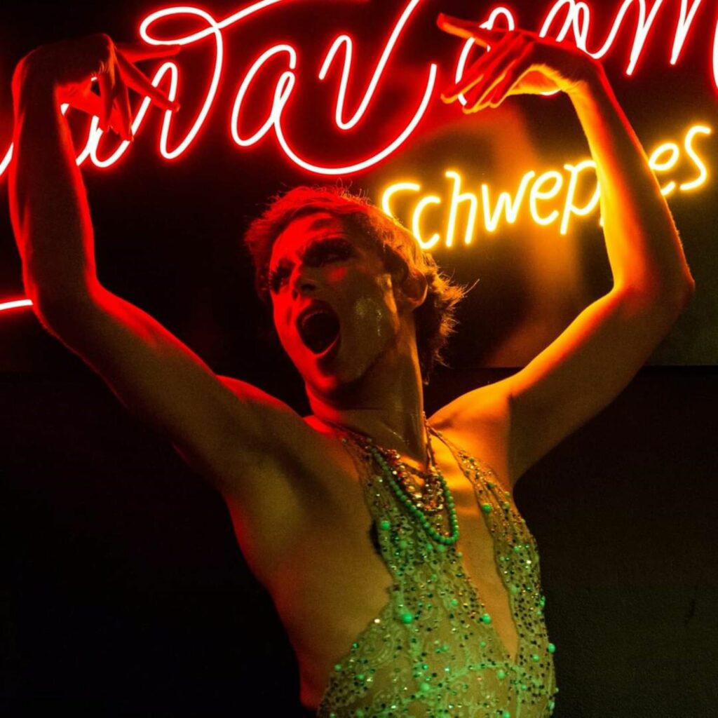 man performing at a burlesque show, neon colors on stage, 