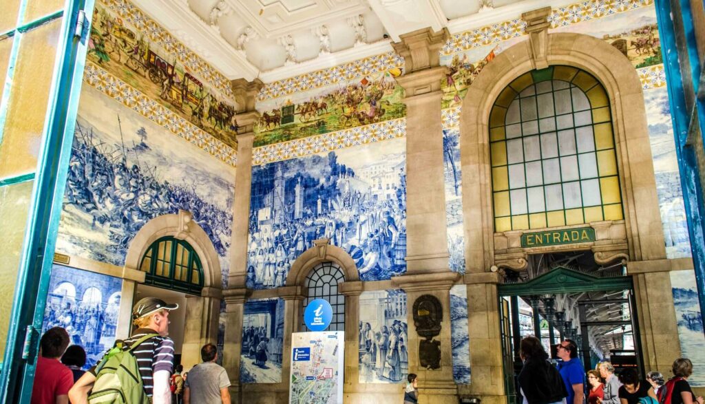 Big room/lounge of a train station with walls covered with blue tiles and stone carved details in the ceiling. 