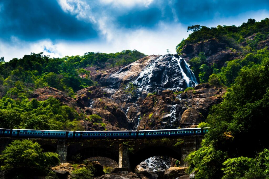 nature reservation in India waterfall on top of a mountain with lush vegetation around it and a train going through a bridge.