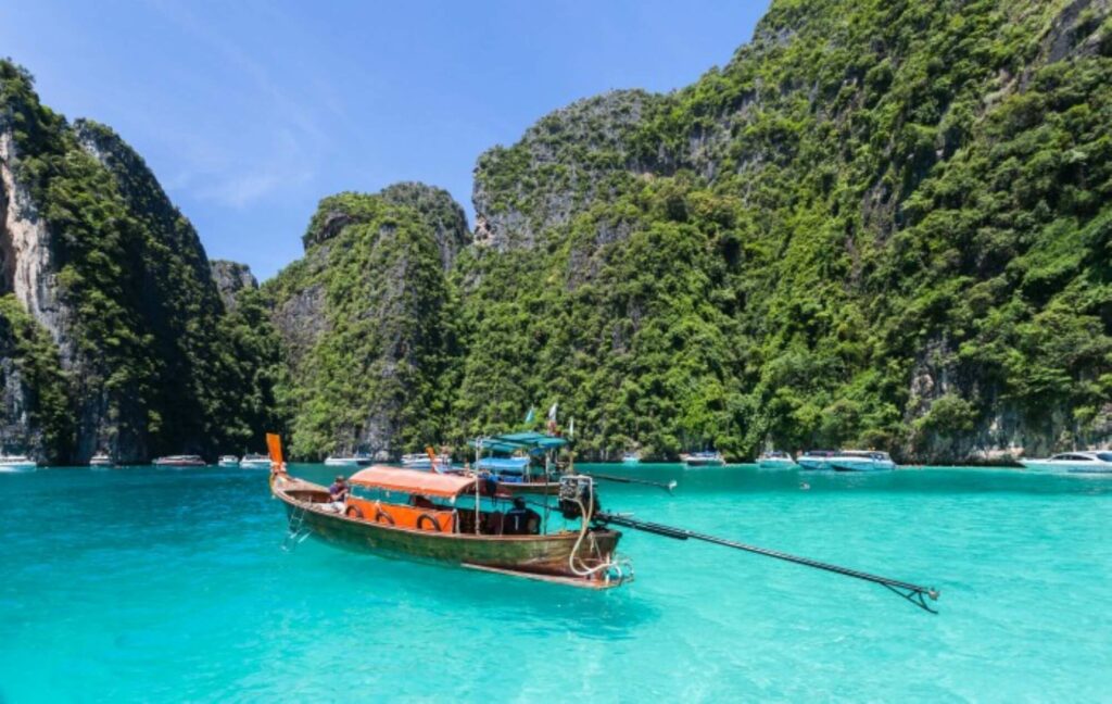 small wooden boat surrounded by lush green hills and floating on beautiful blue and crystal clear waters