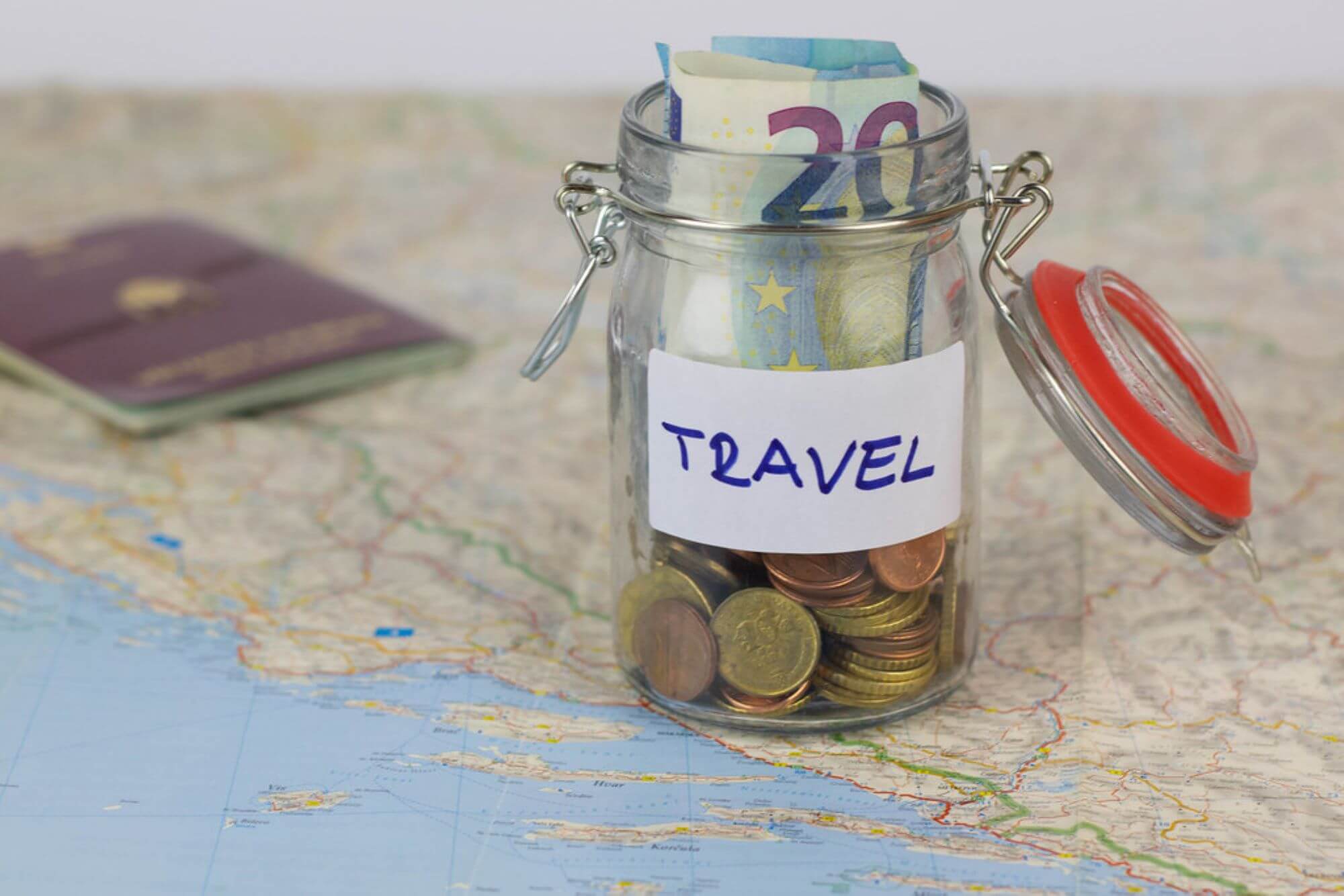 small glass jar with coins and notes inside, on top of a map with a passport by it's side