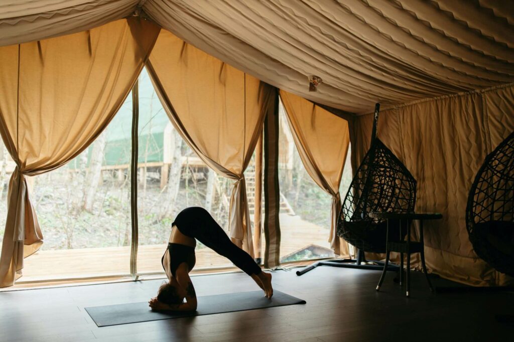 girl doing yoga poses in a room with tent-like decor and nature on the outside